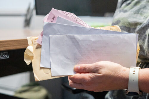 Emily Meyer flips through old bills March 27, 2025, in her office at the Dubois County Community Corrections Center in Jasper, Indiana. She picked up two part-time jobs and often works double shifts on the weekends to afford her daily expenses. (Photo by Alayna Wilkening)